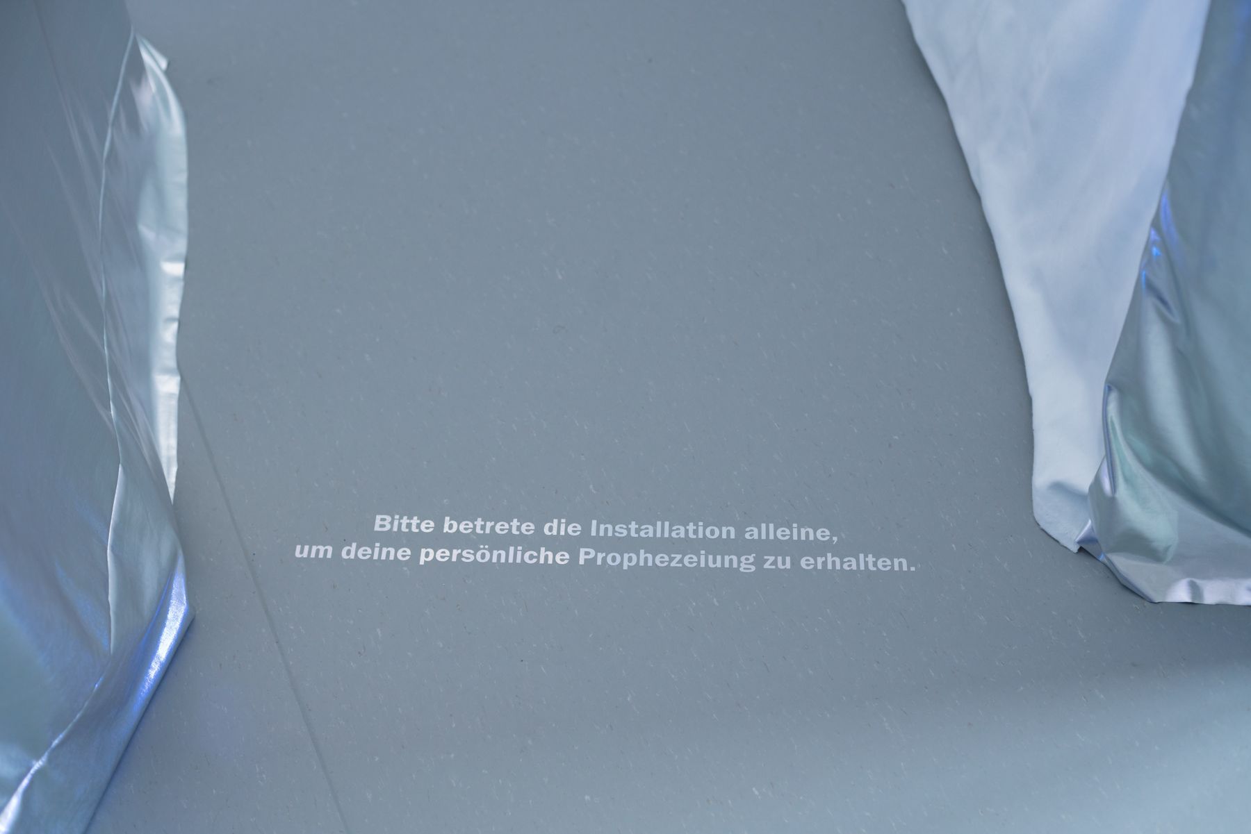 Bodenschrift zwischen silbernem und weißem Stoff am Eingang der Kabine.