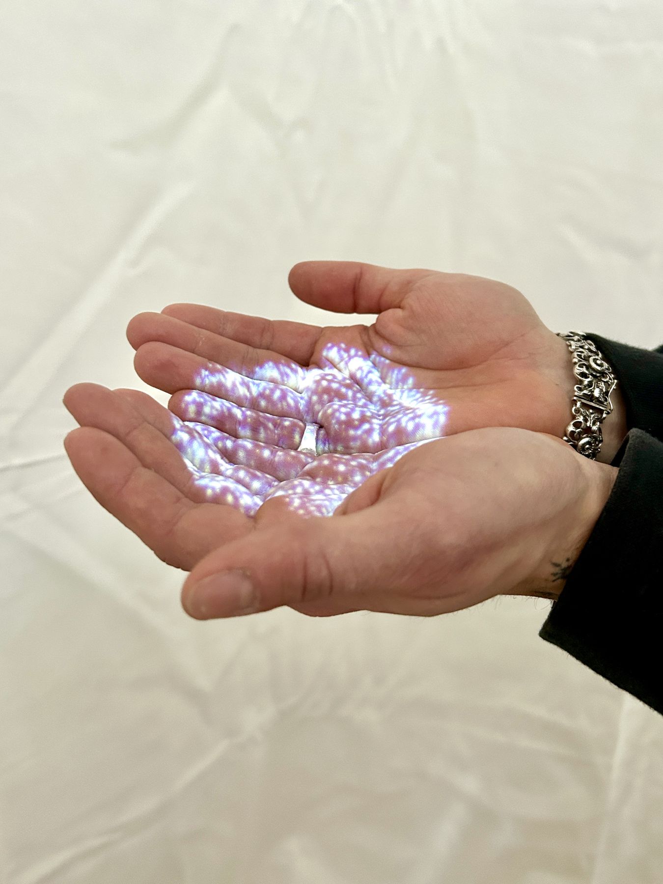 Geöffnete Hände, in denen der projizierte, violett schimmernde Partikel-Orb liegt.